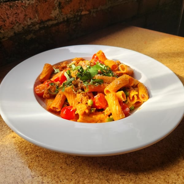 Rigatoni pasta with red sauce, cherry tomatoes, and fresh basil in a white bowl.