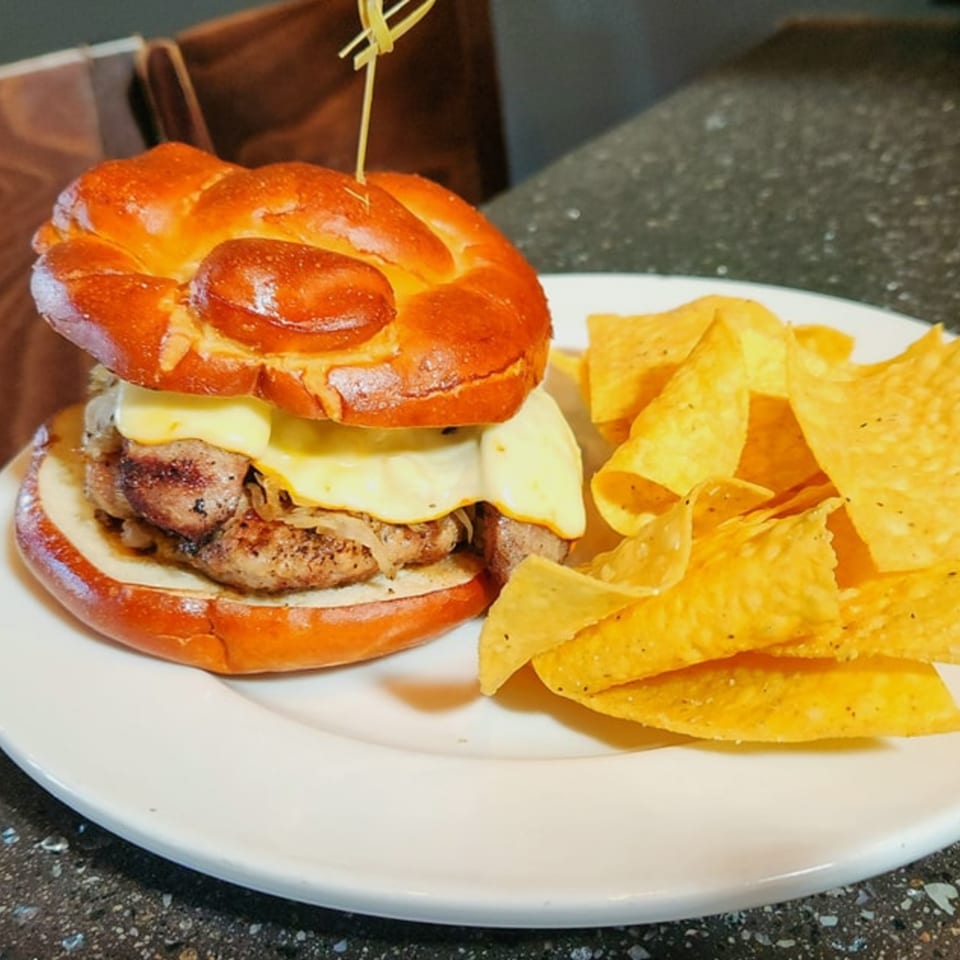 A Wasena City Tap Room & Grill burger with melted cheese and grilled onions, served with tortilla chips.
