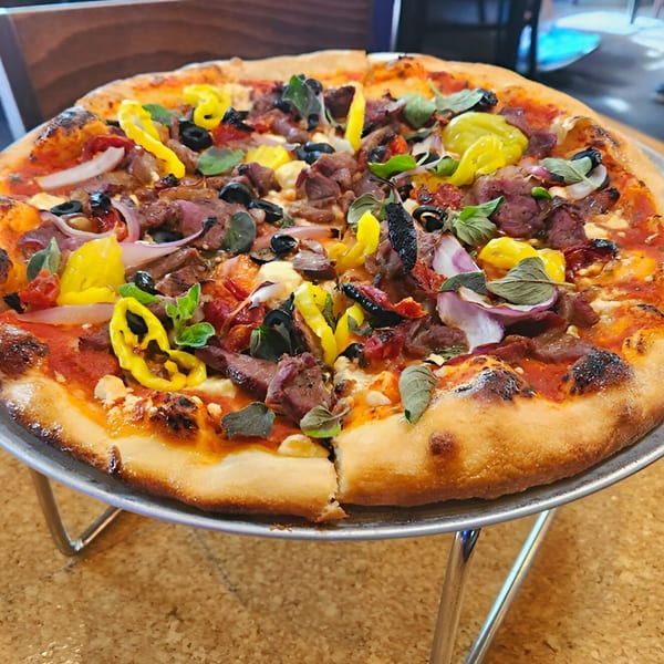 A Wasena City Tap Room & Grill pizza with steak, olives, peppers, onions, and herbs on a stand.