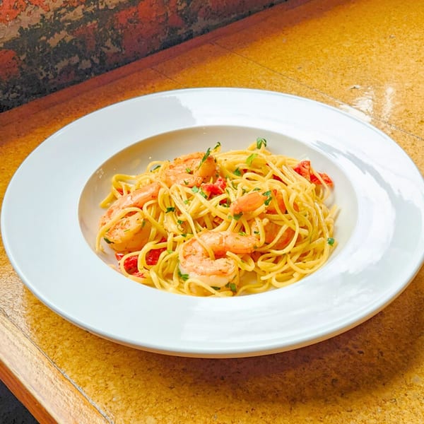 Plate of spaghetti with shrimp, tomatoes, and parsley on a wooden restaurant table.