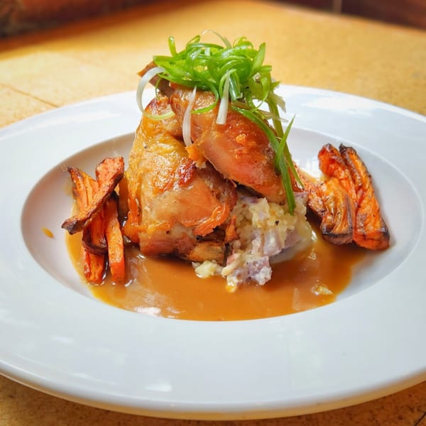 Roasted chicken with mashed potatoes, sweet potato fries, gravy, and green onions on a white plate.