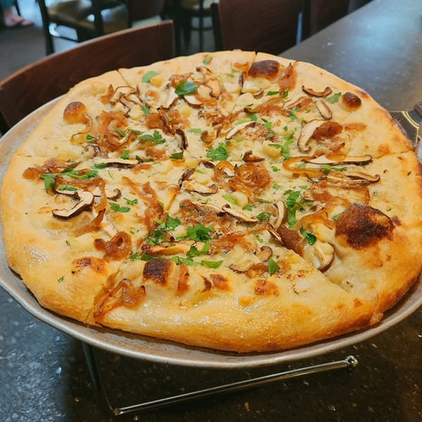 A white pizza with mushrooms, caramelized onions, and fresh parsley on a metal stand.