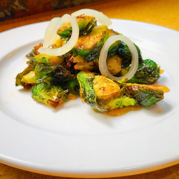 A plate of crispy Brussels sprouts with a sweet glaze and white onion rings.